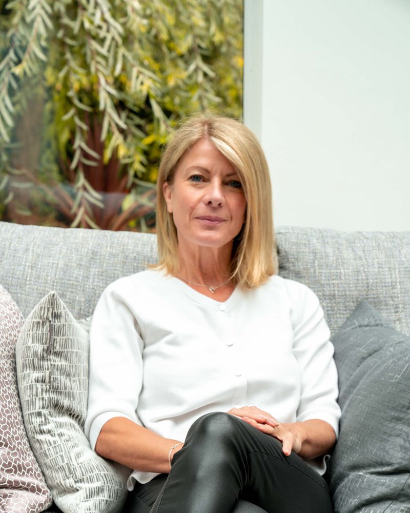 Alexia Bylett, integrative counsellor and coach, sitting on a sofa in a bright garden room