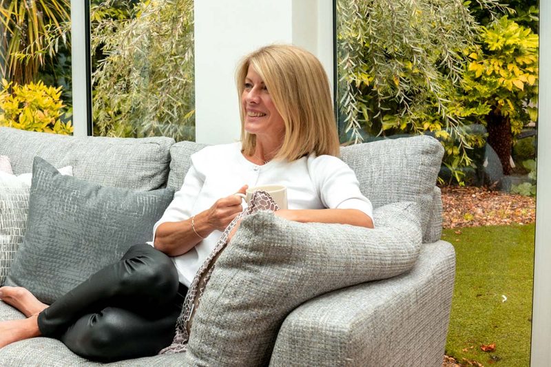 Alexia Bylett smiling on a sofa in a light, plant-filled room