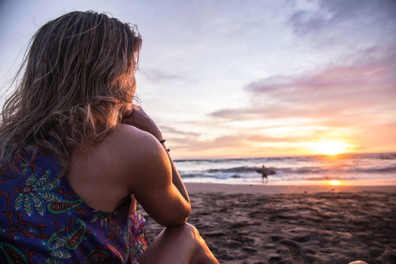 A woman sitting on a beach watching the sunset